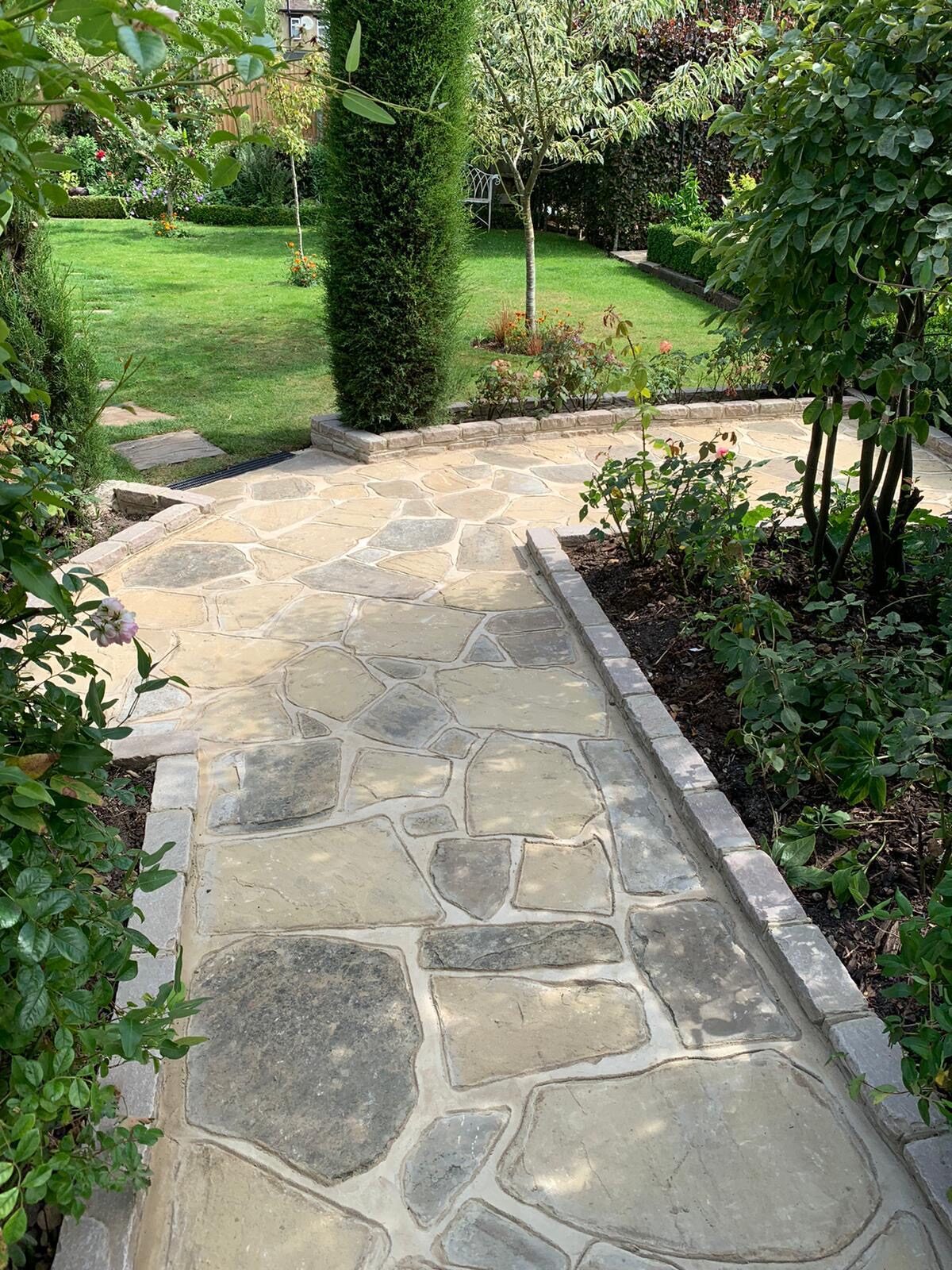 Landscaped garden with sandstone path, borders and fencing in Surrey